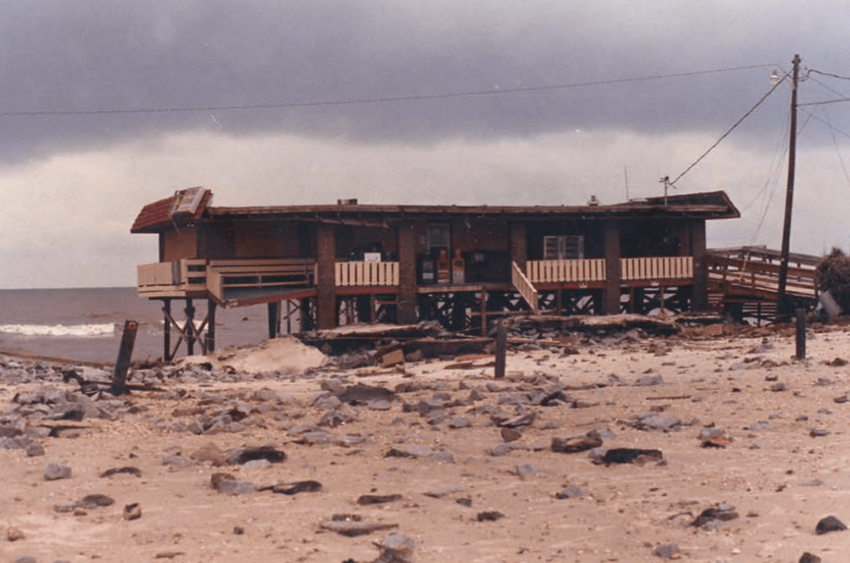 a damaged wooden structure on the beach with storm clouds in the background