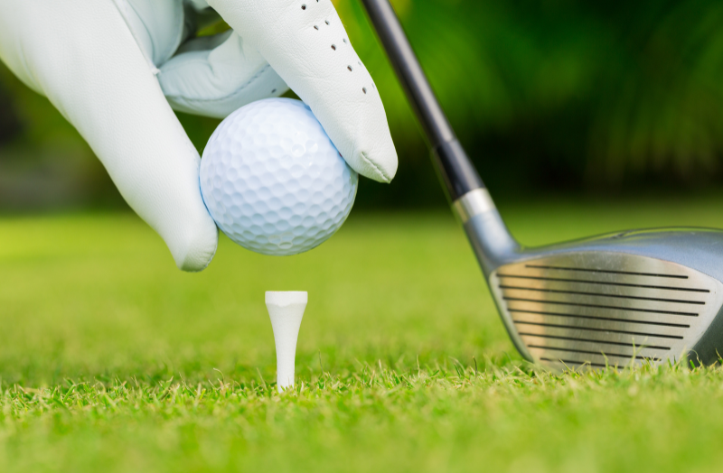 Gloved hand placing a golf ball onto a tee