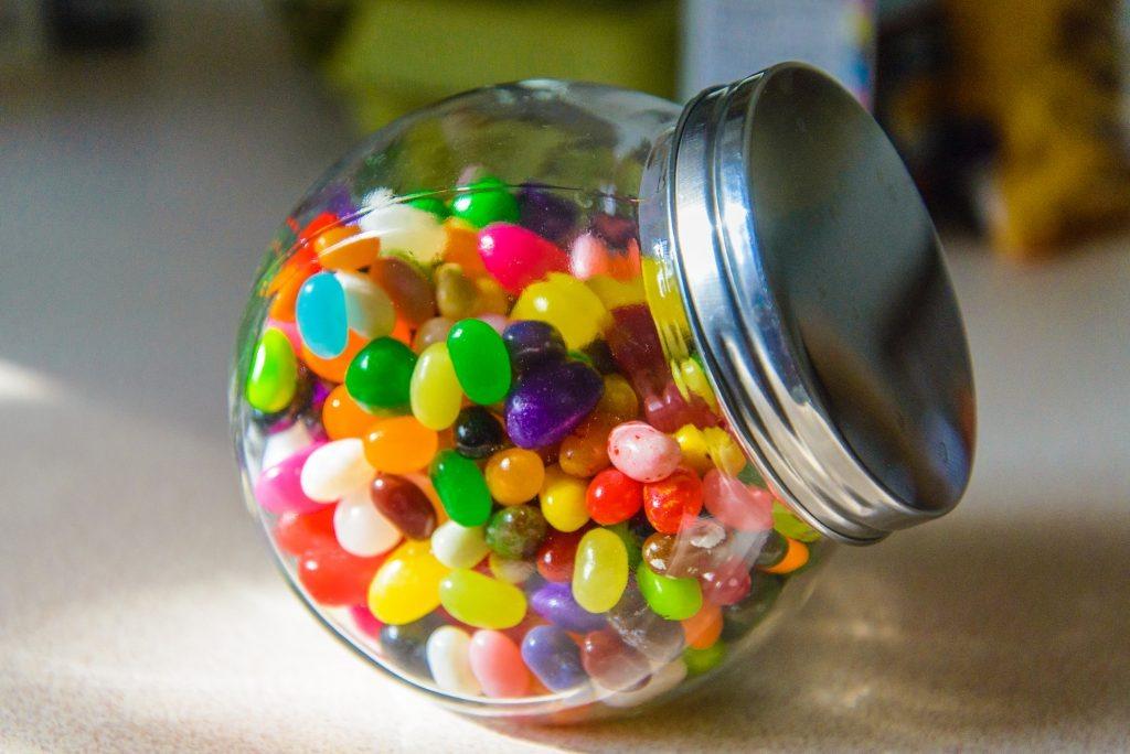 a clear jar of jelly beans with a silver lid.