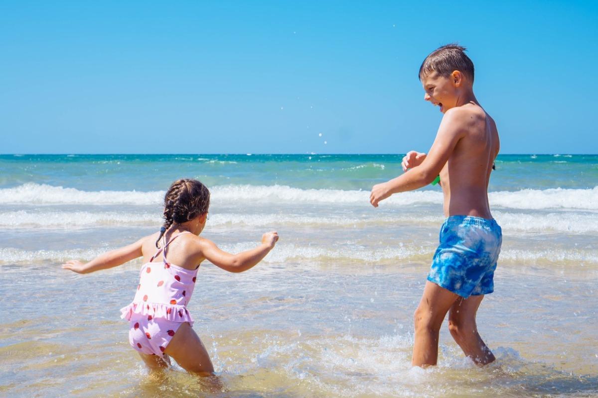 Children, brother and sister, go into sea on sunny beach. Sun and sea, splashes of water. Tourism and travel. Happy childhood.