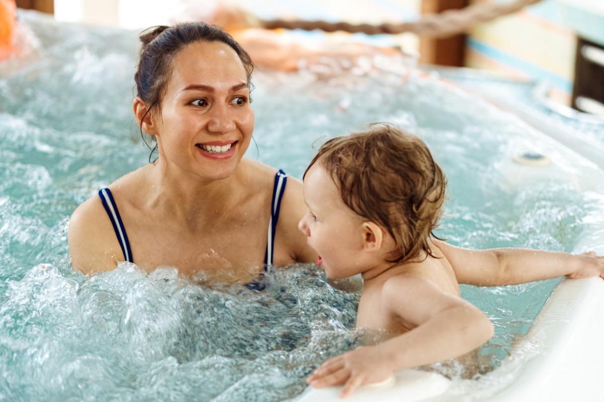 Cheerful woman with little child swim together in whirlpool bath.
