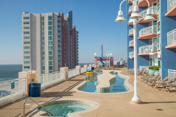 Oceanfront hotel pool area with loungers, hot tub, and clear blue sky.