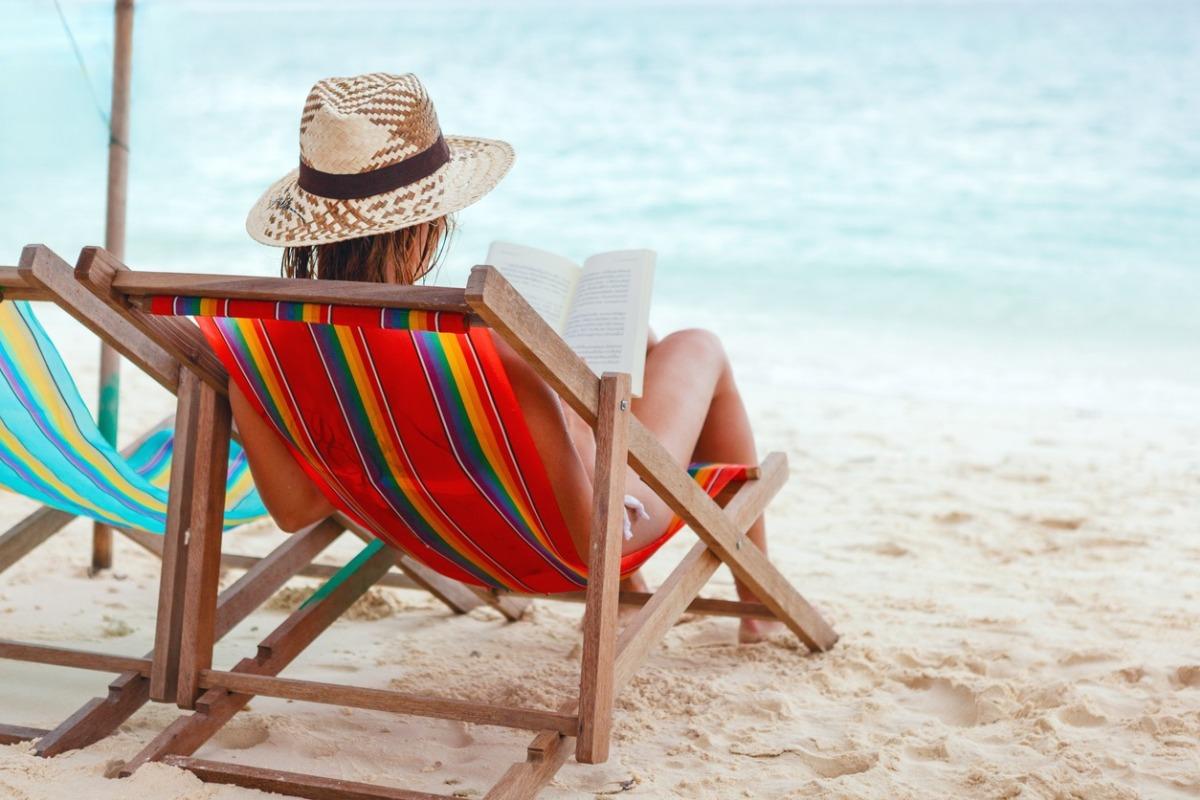 a woman on a beach in a chair reading a book she's gotten from Little Free Libraries